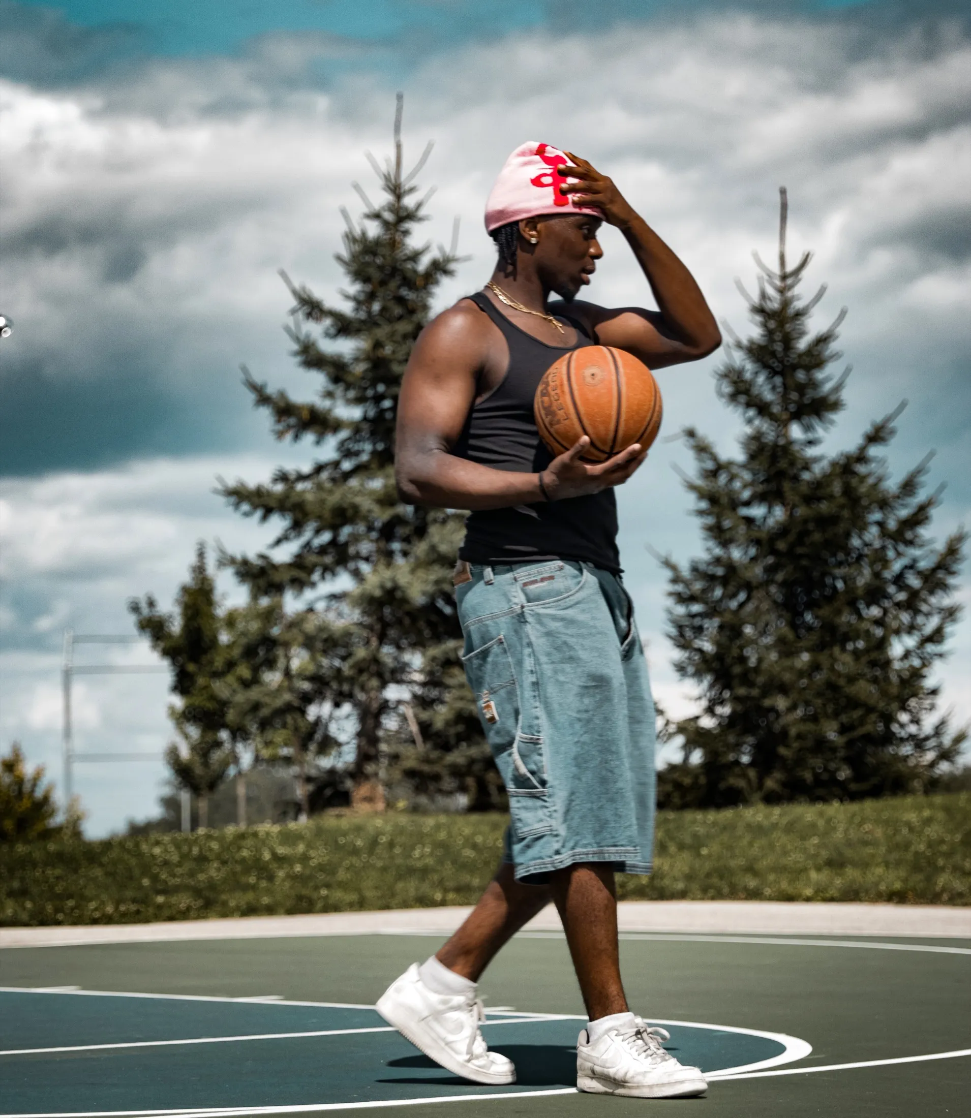 Athlete holding a basketball on an outdoor court under a dramatic sky.
